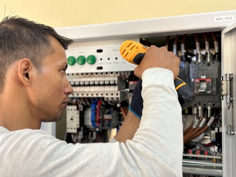 commercial-plumbing Professional electrician using a drill on an indoor circuit breaker panel.